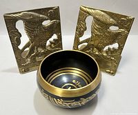 Photo showing pair of brass eagle bookends and black brass singing bowl.