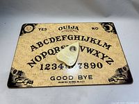 Top view of vintage Ouija board with alphabets, numbers, yes and no, good bye, artistic corners and planchette in center.