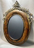 Front view of vintage oval mirror showing wooden frame with metal leaf decoration and beveled glass.