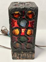 Front view of the lamp showing the colorful stained glass and textured black framing with wood base and electrical cord.