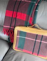 Folded wool blanket and matching zippered carrying case on a gray leather sofa.