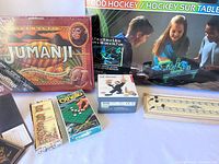 Photo showing Jumanji board game box, Othello game box, cribbage board, a small figure, and glow-in-the-dark rod hockey table visible in the background