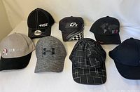 Seven assorted ball caps arranged on a white background showing front and top views, displaying brand logos and designs.