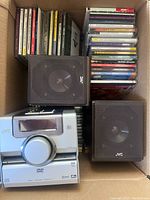 Top view of the JVC CD player, two speakers, and a box full of assorted CDs showing a variety of artists in jewel cases.