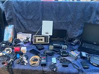 Overview of all electronics including Dell laptop, Realistic cassette deck, GPS, kitchen scale, various portable players, and accessories spread on a towel.