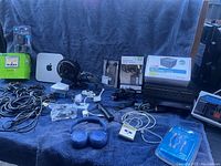 Wide shot of the lot showing various electronics including Apple Mac Mini, Sony cassette deck, JBL headphones, TomTom GPS and scale, cables, docking station, small fan and other miscellaneous items.