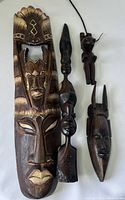 Four wood carvings shown together on a white surface including two figurative statues and two mask carvings.
