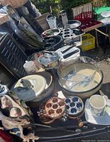 Photo showing assortment of kitchen items including pottery dishes, muffins pans, glass bowls, and utensils on display outdoors.