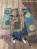 Three dyed rayon sarongs laid flat showing different colors and patterns with tasseled edges