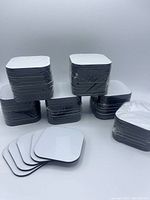 Six stacks of ten blank square coasters each, showing gloss white tops and black backs, 3x3 inches, rounded corners