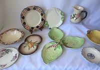 Front view of all nine china items showing their shapes, colors and designs on white surface.