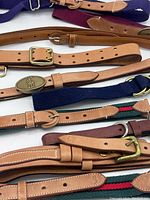 Photo showing multiple leather belts in tan, brown, navy blue, and maroon with various buckle styles including brass and silver-tone.