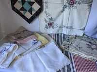 Photo of assorted linens including folded embroidered tablecloths, napkins, and woven striped linen.