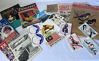 Photo showing the assortment of vintage magazines, newspapers, stickers, pin-up images, and postcards spread out on white background.