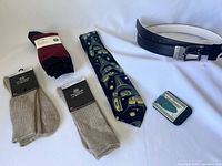 Full lot showing two pairs of socks, patterned necktie, black leather belt with silver buckle, and a money clip.