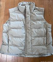 Front view of light beige men's goose down puffer vest by Lululemon with zipper and snap button closure on hardwood floor.
