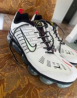 Front and side angle showing left shoe with visible Nike swoosh in black with pastel gradient outline, ribbed white upper, black laces, and red heel tab.