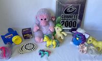 Photo showing the full collection including a purple Ty Beanie Baby monkey, several My Little Pony toys in yellow, green, and purple, the Guinness World Records 2000 book, ViewMaster projector and reels, Slinky toy box, and an original Furby toy.