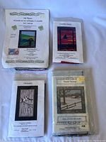 Four quilt kits in packaging, showing front instructional covers for each design: Celtic Whispers, Chickadees, Canadian Sunset, Snow Scene