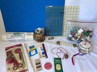 Wide angle photo showing all sewing supplies laid out on blue cutting mat, including thread spools, rulers, measuring tape, tins, scissors and pin cushions.