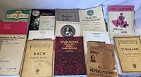 A spread of 12 assorted vintage sheet music books laid out, showing various composers like Bach, Cesar Franck, Schumann, and thematic titles such as Pink Panther.