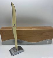 Vancouver 2010 Olympic torch replica assembled on metal display base with Canadian birch wood box behind it with metal accent and Olympic logo.