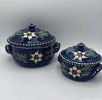 Two vintage ceramic nesting pots with lids, dark blue with floral decorations and handles visible.