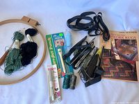 Photo showing weaving and crochet tools and supplies including yarn, needles, spools of thread, elastic bands, weaving cards, and a pattern book.
