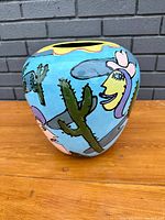 Front angled view showing vivid blue background and painted cacti, human faces with hats, and abstract shapes