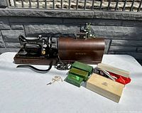 Photo showing the Singer sewing machine set out with the original wooden case, key, and multiple boxes of attachments and accessories.