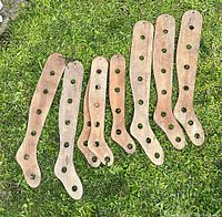 Eight antique wooden sock stretchers lying on grass, showing full length and hole patterns