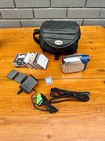 Full lot photo showing Canon ZR-800 camcorder, carrying case, multiple 8mm videotapes, power adapter, AV cables, and memory card on wooden table.
