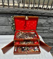 Open wooden jewelry box showing three tiers and red fabric lining filled with mixed jewelry