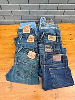 Several pairs of jeans laid flat showing back pockets and leather brand patches including Levi's and other brands.