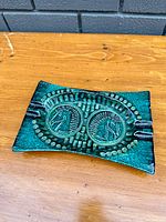 Top and angled views of the blue glazed rectangular pottery ashtray with embossed horse head designs and decorative textured surface.