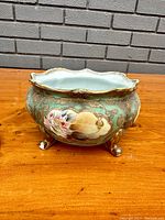 Front view of an oval-shaped Nippon porcelain bowl with scalloped rim, hand painted floral design, gold leaf accents, and footed base on wood surface.