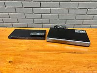 Panasonic Viera Tuner box and Panasonic Blu-ray player placed on wooden table in front of grey brick wall, showing top view and remote control on the tuner box.