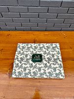 Box for an oval tilt-top table with floral patterned design and Bombay Company logo on top.