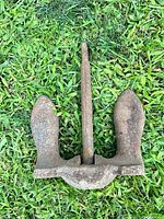 Top-down view of the vintage cast iron boat anchor showing overall condition and shape on grass background.