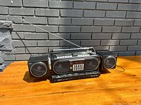 Front view of vintage AKAI PJ-W30 boombox with two detachable speakers on wooden surface against brick wall.