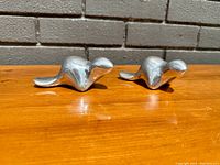 Two identical smooth pewter beaver figurines on wooden surface, showing front and side profiles
