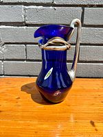 Front angle view of cobalt blue glass pitcher with silver-tone metal handle and decorative metal accents near the spout.