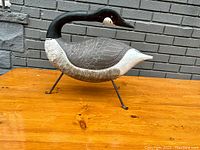 Front view of full-bodied decoy on wooden surface against brick wall.