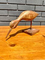 Front and side view of a hand-carved wooden shore bird mounted on a square wooden base, showing natural wood grain and primitive carving style.