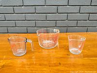 Three vintage measuring cups on wooden surface against brick background