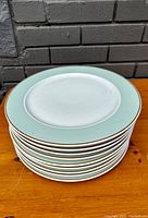 Stack of 12 porcelain dinner plates with mint green and gold rim design.