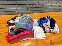 Wide view of assorted scarves folded in boxes on wooden table with brick wall background.