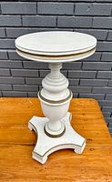 Front view of the vintage turned wood plant stand showing the eggshell white paint and gold trim along base and central column.