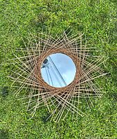 Top view of the mirror laid on grass, showing the circular glass and decorative twig starburst frame.