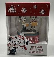 Front view of the Disney Mickey and Minnie holiday snow globe in original packaging, showing the figurines with songbooks and snowman, and marked 2021 on the base.